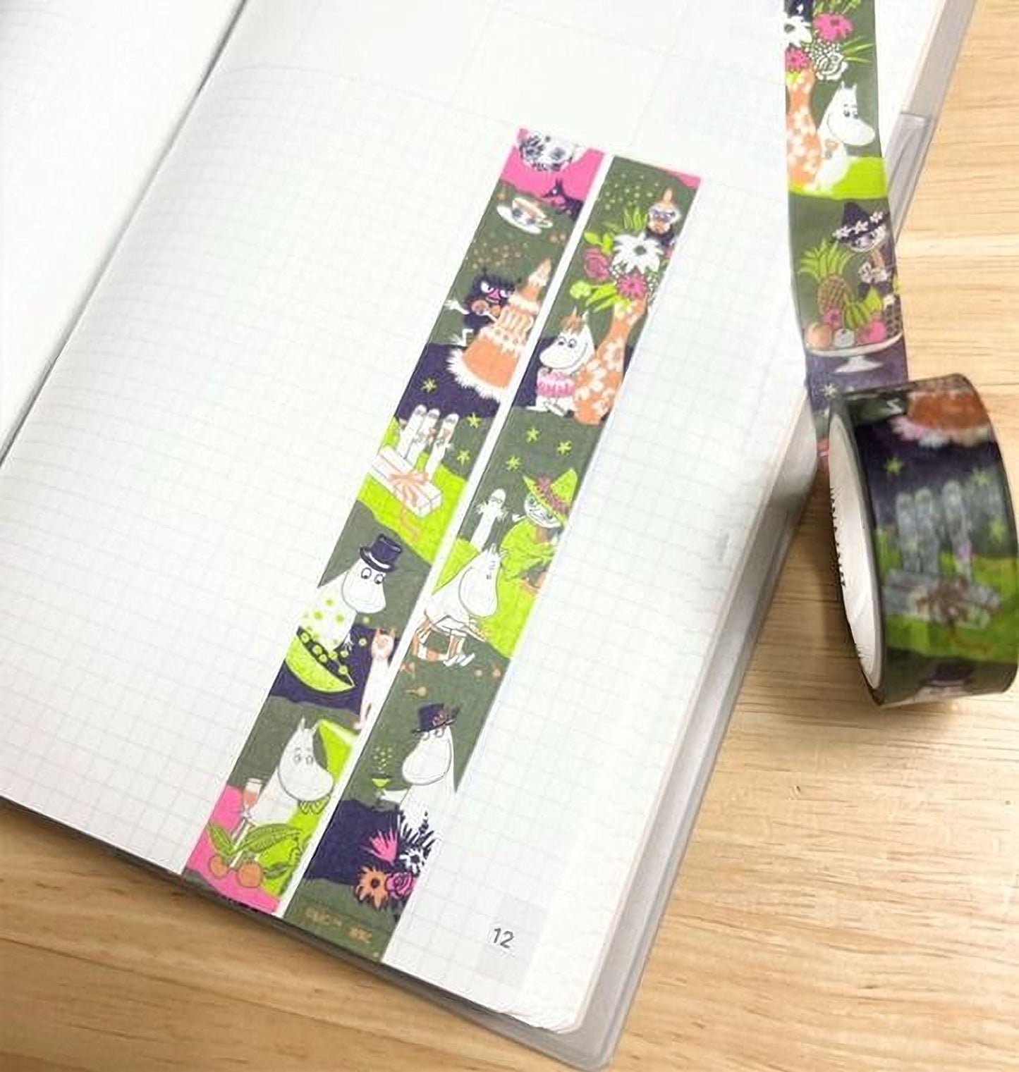 A notebook with a colorful, patterned tape on it, and a roll of tape lying next to it on a wooden surface.