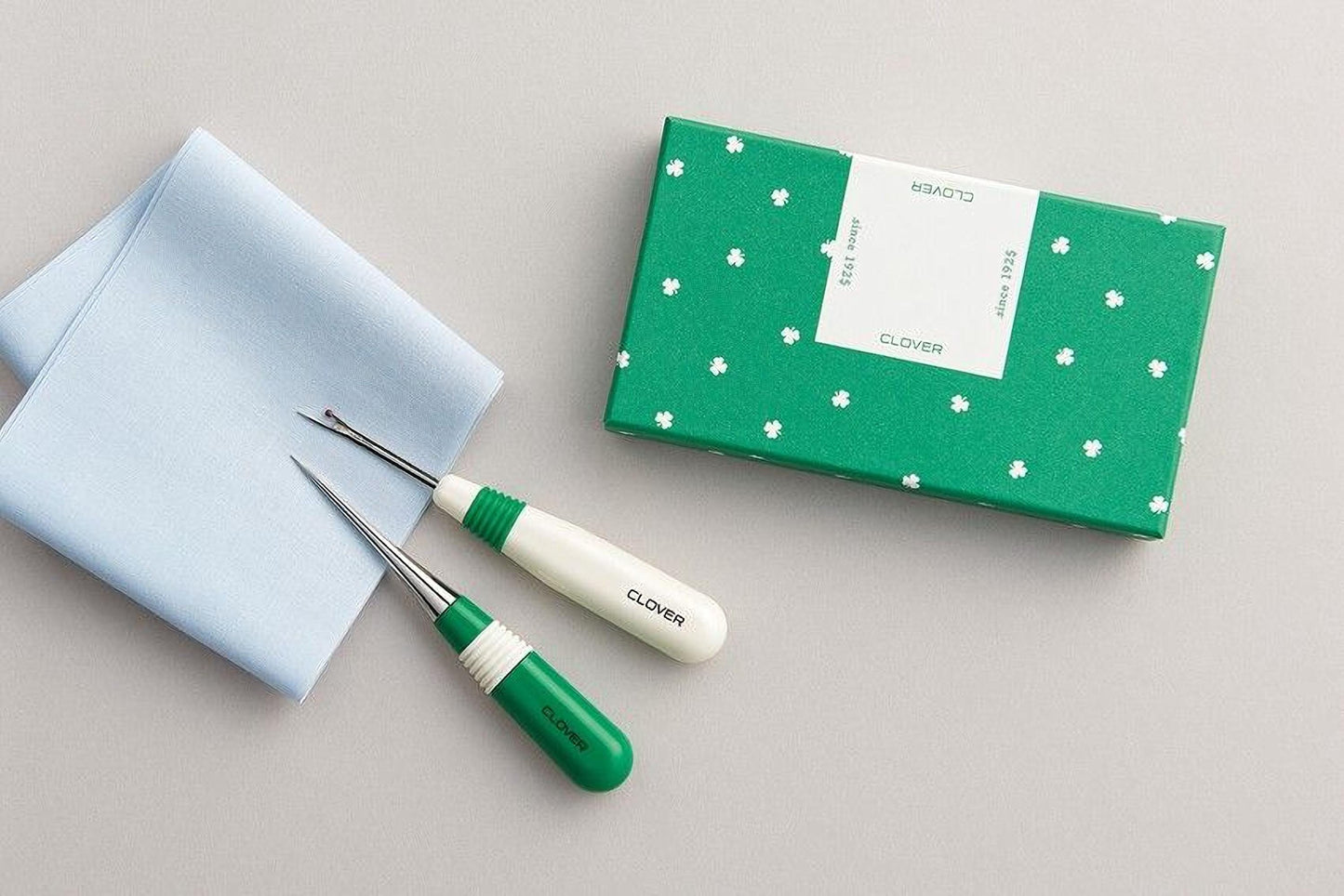 a pair of green and white sewing tools, a box with a green and white pattern, and a light blue cloth.
