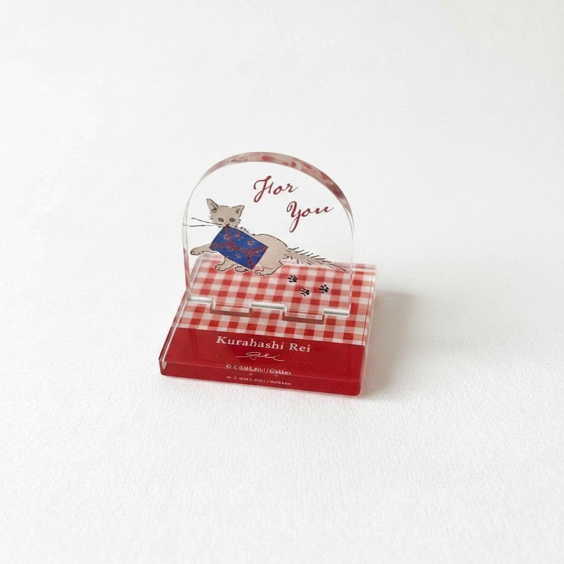 A clear glass stand with a red and white checkered pattern, featuring a cat illustration and the text "Kurahashi Rei" on it.