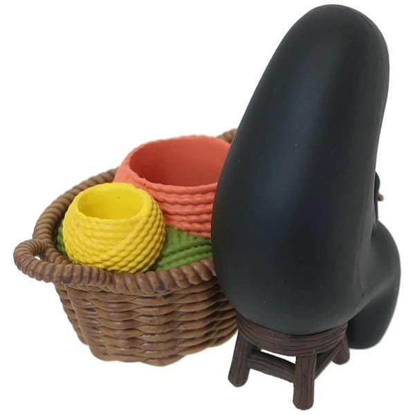 a black object sitting on a brown wicker basket, which is filled with various colorful objects, including a yellow ball, a red bowl, and a green bowl.