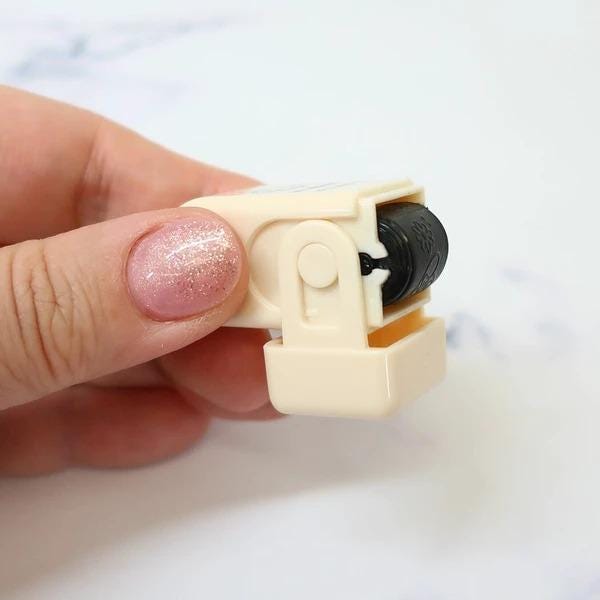 A hand holding a small, beige-colored object with a black roller attached to it.