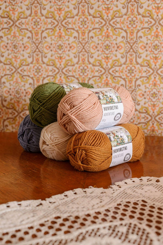 a collection of colorful yarn balls, including green, pink, and orange, arranged on a wooden surface. The background features a patterned wallpaper.