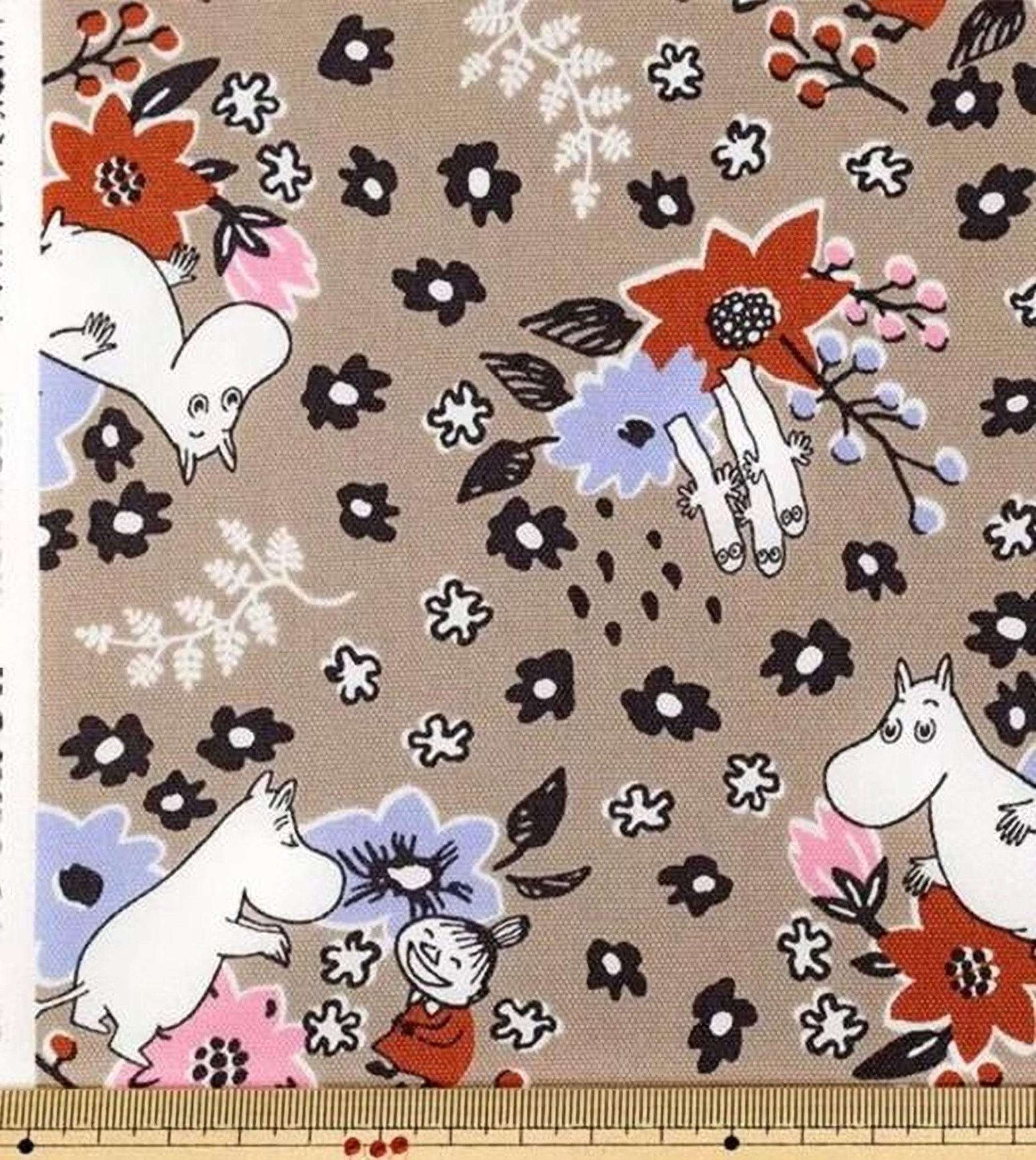 a fabric with a floral pattern and various cartoon-style characters, including Moomo, a character from the Moomo family. The fabric appears to be a piece of clothing or textile, with a ruler for scale.