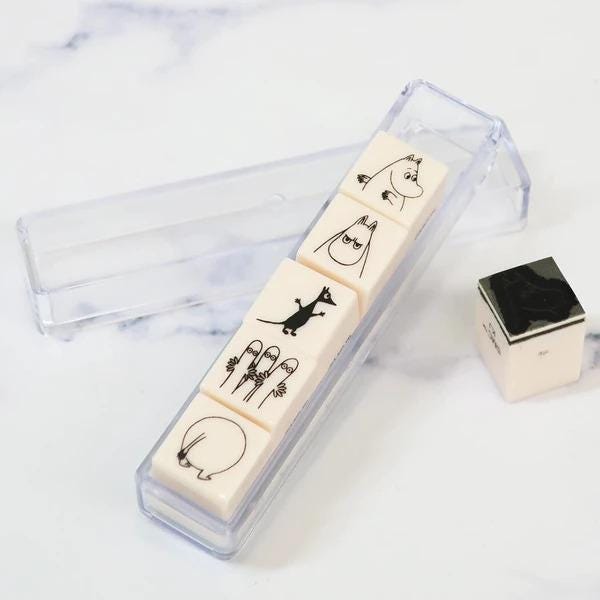 A clear plastic container with four white square tiles featuring black illustrations of cartoon-like characters, including a cat, a dog, and a bird.