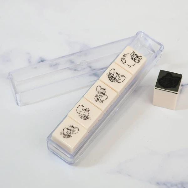 A set of five small, square-shaped objects with cartoon-like images on them, placed in a clear plastic container.