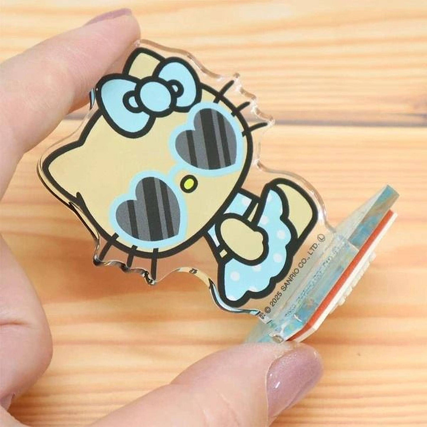 A hand holding a clear plastic figurine of a Hello Kitty character with heart-shaped sunglasses.