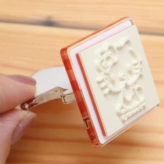 A hand is holding a Hello Kitty stamp in a wooden surface.