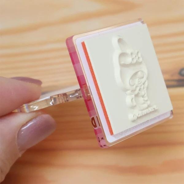 A hand holding a clear stamp with a white image of a cartoon character on it.