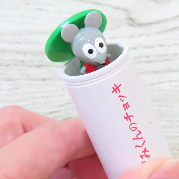 A small toy mouse with a green hat is sitting inside a white tube with red text on it.