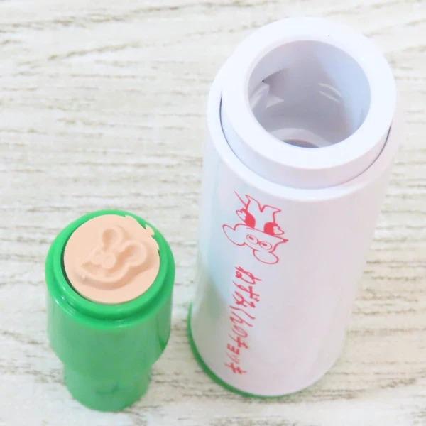 a white cylindrical container with a red and pink design, and a green container with a similar design on a white surface.