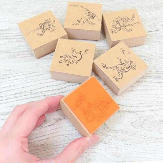 A hand is holding a wooden stamp with an orange design on it, surrounded by several other wooden stamps featuring animal designs.