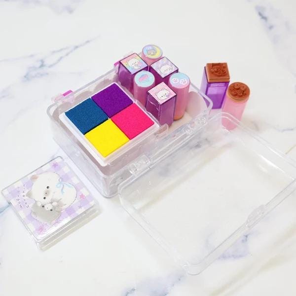 A clear plastic container with a lid, containing various colorful stamp blocks and a small picture frame.
