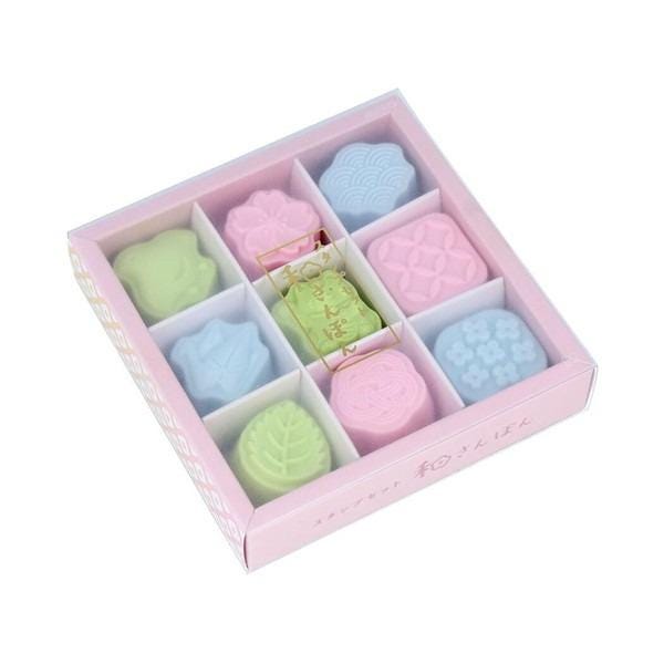 A pink box containing nine colorful, pastel-colored sweets arranged in a 3x3 grid.