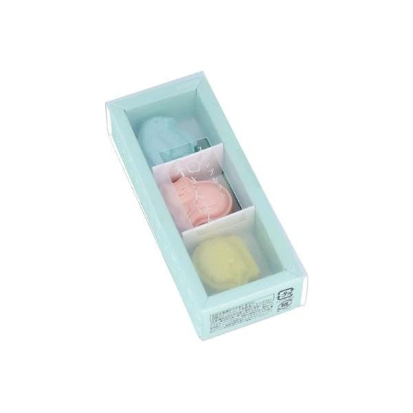 A light blue rectangular box containing three small, colorful objects, likely soap or skincare items.