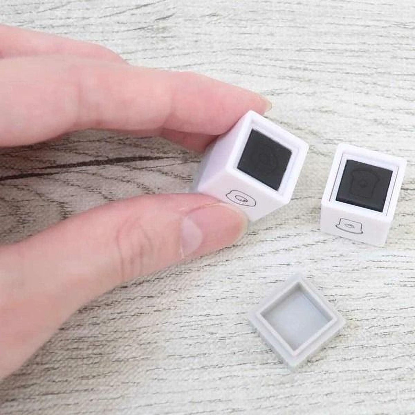 A person's hand is holding two small white cubes with black markings on a wooden surface.