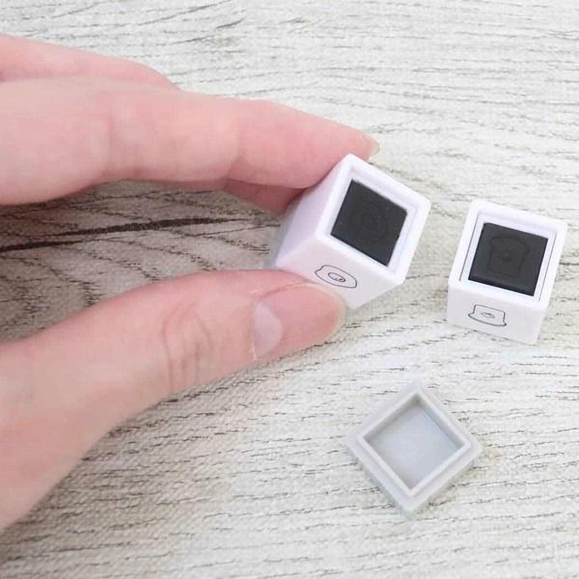 A person's hand is holding two small white cubes with black markings on a wooden surface.