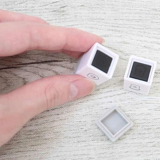A person's hand is holding two small white cubes with black markings on a wooden surface.
