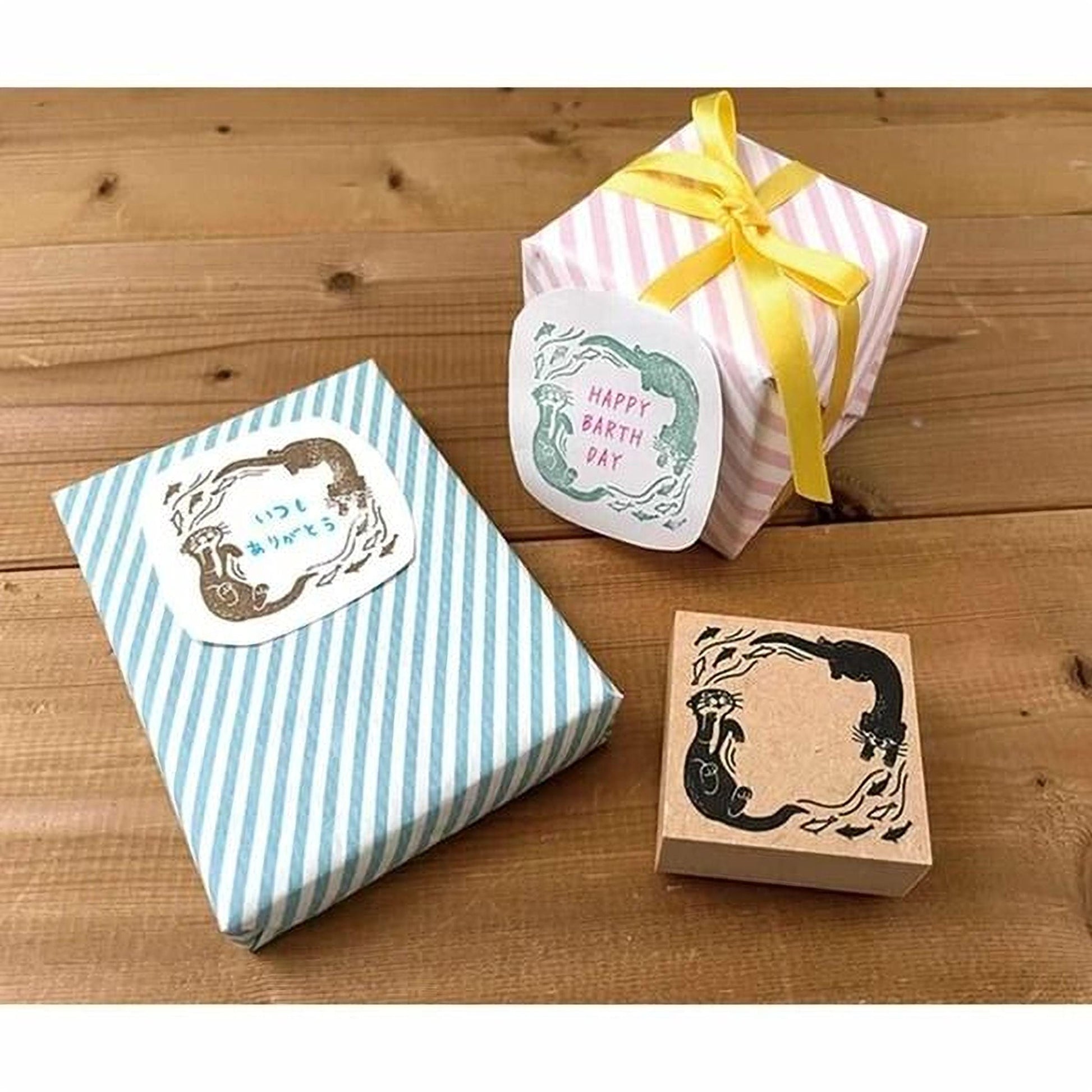 a wooden surface with three wrapped gifts and a stamp. The gifts are wrapped in blue and white striped paper, and one of them has a yellow ribbon tied around it. The stamp is a simple black and white design.