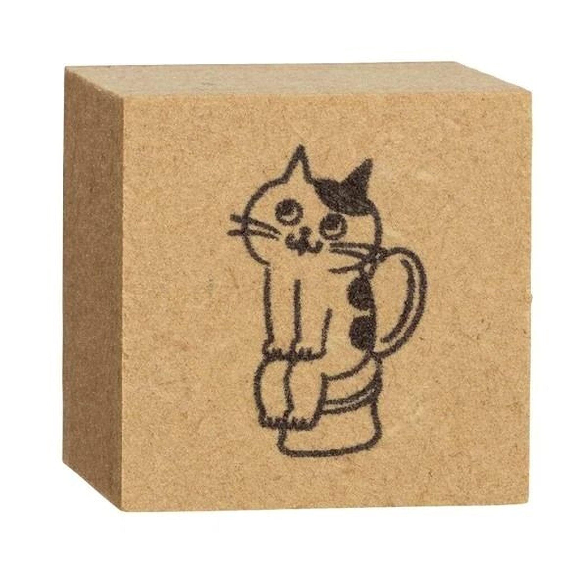 A square wooden block with a black and white drawing of a cat sitting on a toilet.