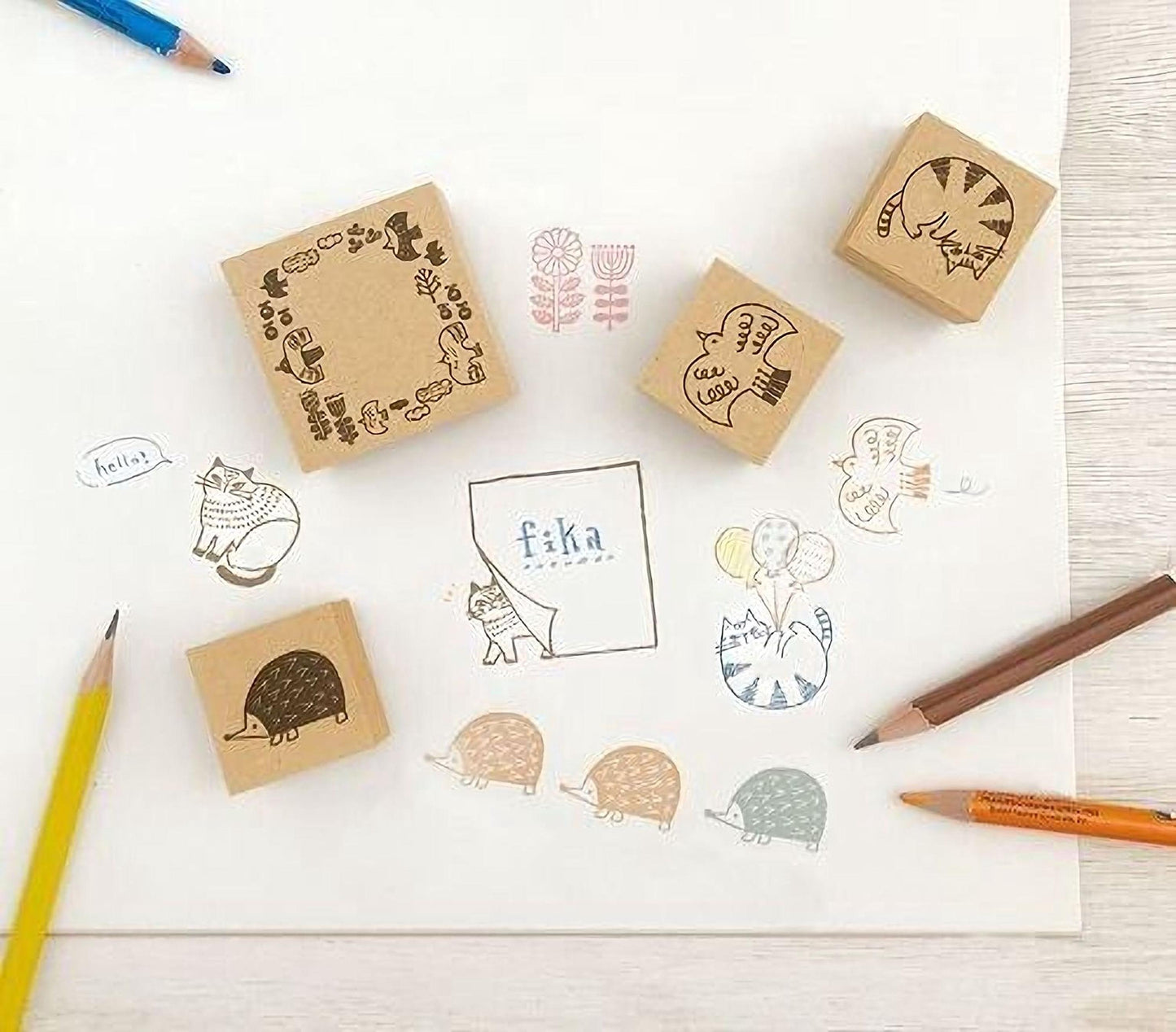 A collection of various stamp designs, including cats, flowers, and other whimsical illustrations, along with some colored pencils and a piece of paper.