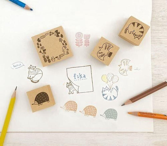 A collection of various stamp designs, including cats, flowers, and other whimsical illustrations, along with some colored pencils and a piece of paper.