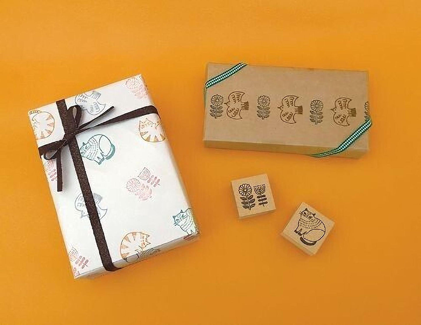 a gift box with a bow, a brown box with a green ribbon, and three rubber stamps with cat designs on a yellow background.