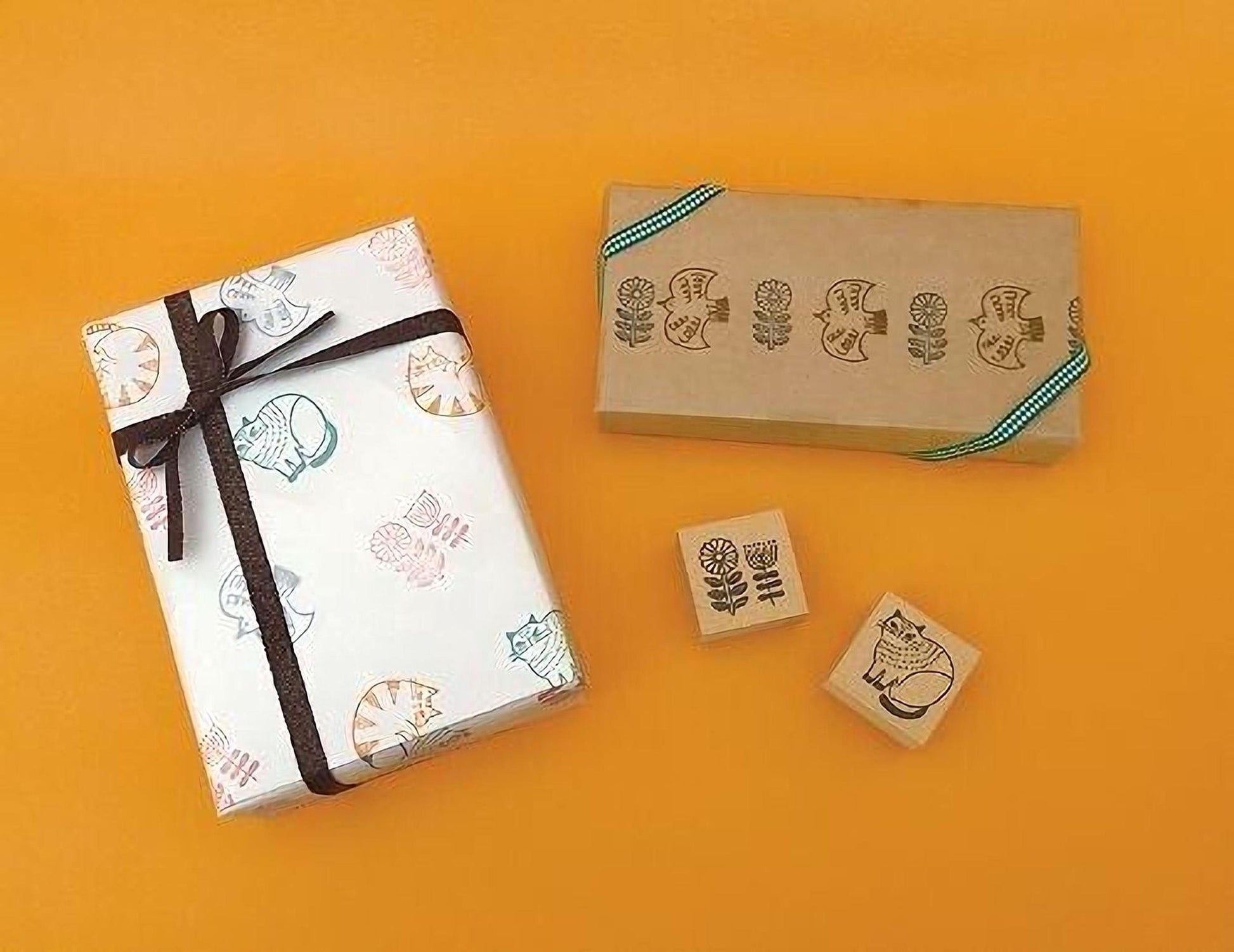 a gift box with a bow, a brown box with a green ribbon, and three rubber stamps with cat designs on a yellow background.