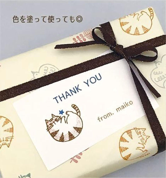 A gift box wrapped with a brown ribbon and a white card with a cat illustration, along with Japanese text that says "Thank you from miko".