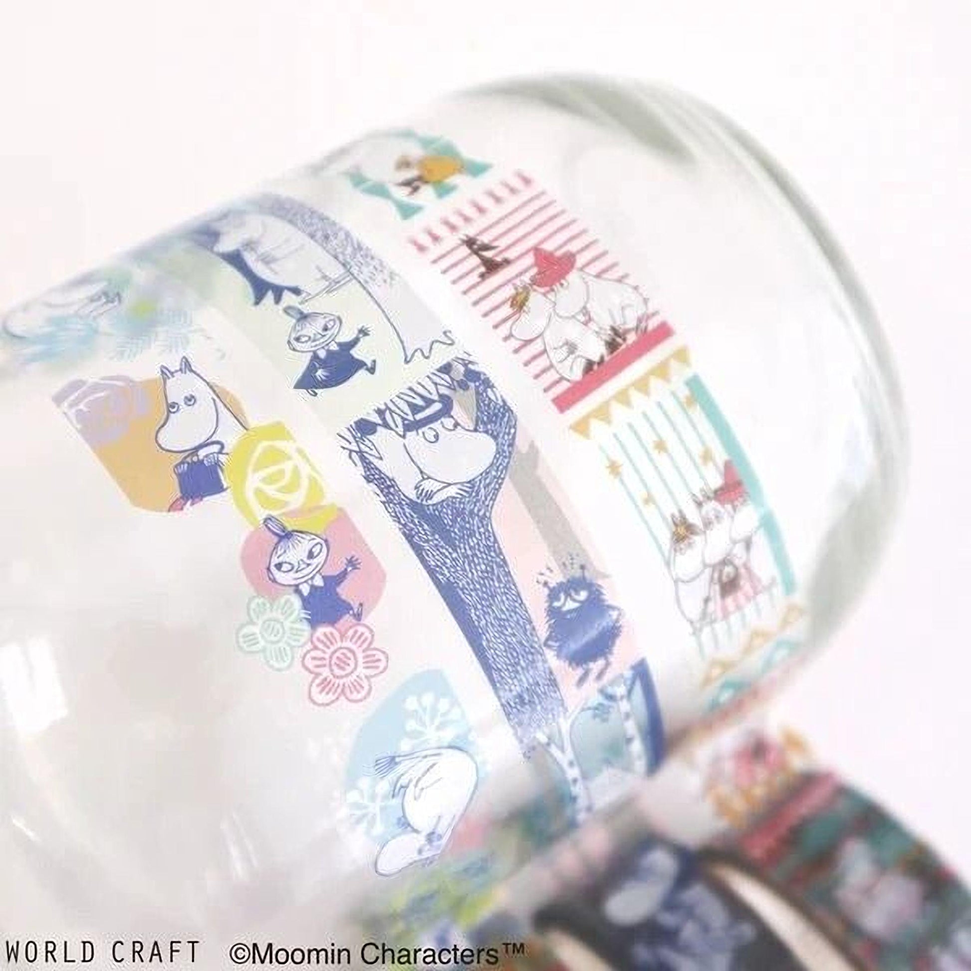 A close-up view of a glass mug with a colorful, patterned design featuring various cartoon characters and illustrations.