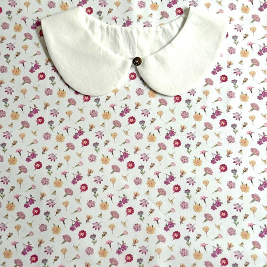 a white collar with a button, placed on a white fabric with a floral pattern.