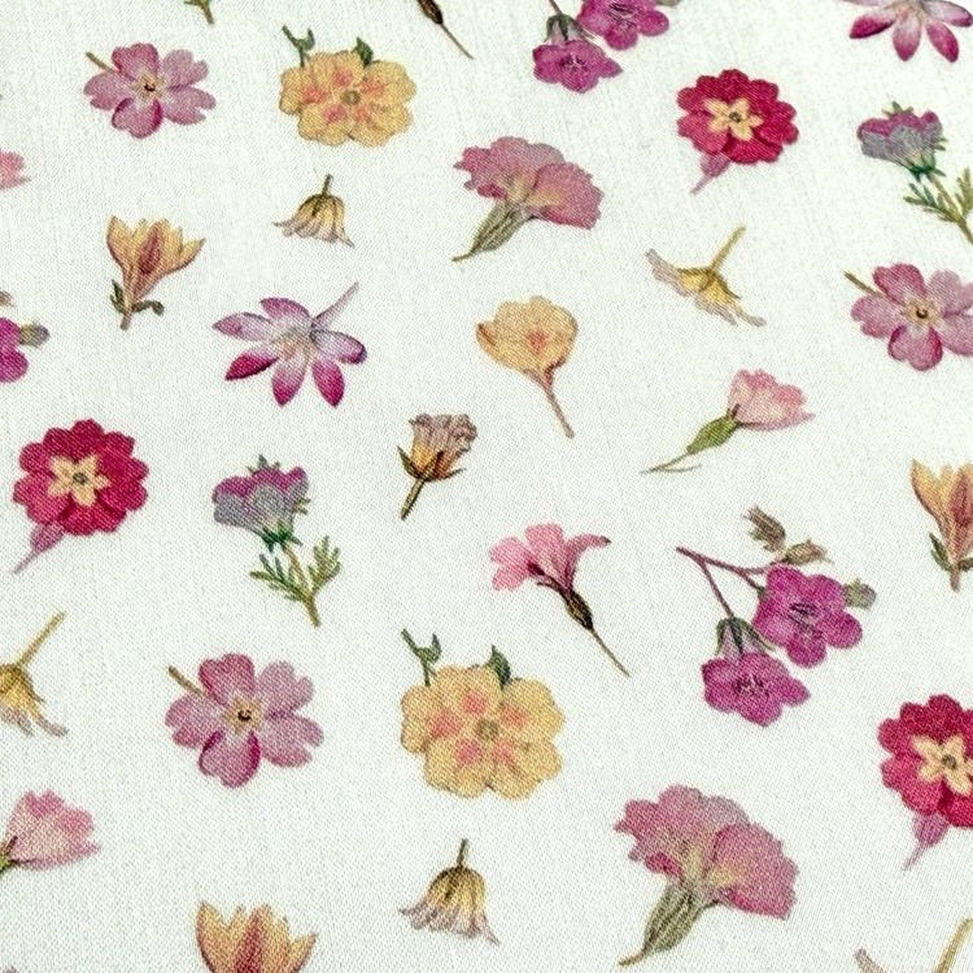 a close-up view of a white fabric with a repeating pattern of various colorful flowers, including pink, yellow, and purple flowers.