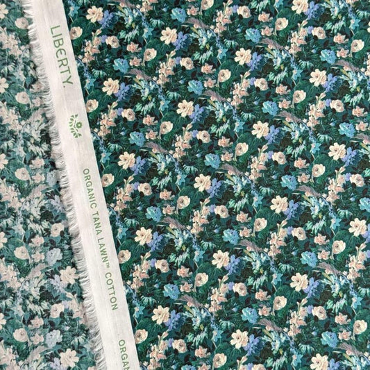 a close-up view of a fabric with a floral pattern, including various shades of green, blue, and white flowers. The fabric appears to be a type of cotton material, as indicated by the text "Liberty ORGANIC TAN LAWN COTTON" visible on the fabric.