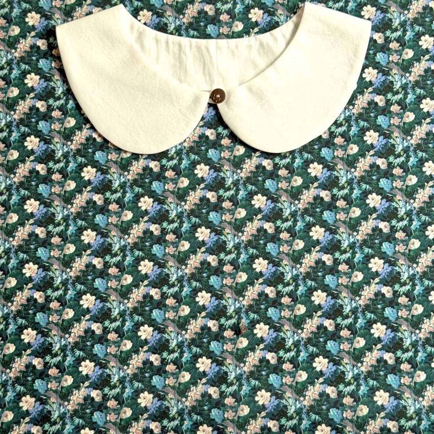 a white collar with a button, set against a background with a floral pattern.