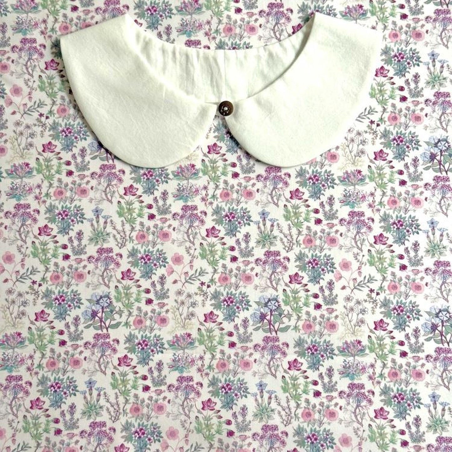 a white collar with a button, placed on a floral print fabric.
