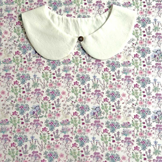 a white collar with a button, placed on a floral print fabric.