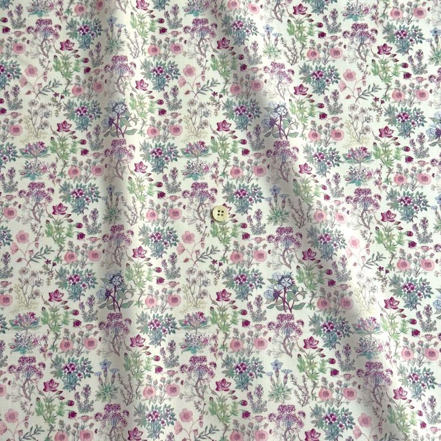 a fabric with a repeating floral pattern in shades of pink, green, and white. The pattern consists of various flowers and leaves, creating a visually appealing and intricate design.