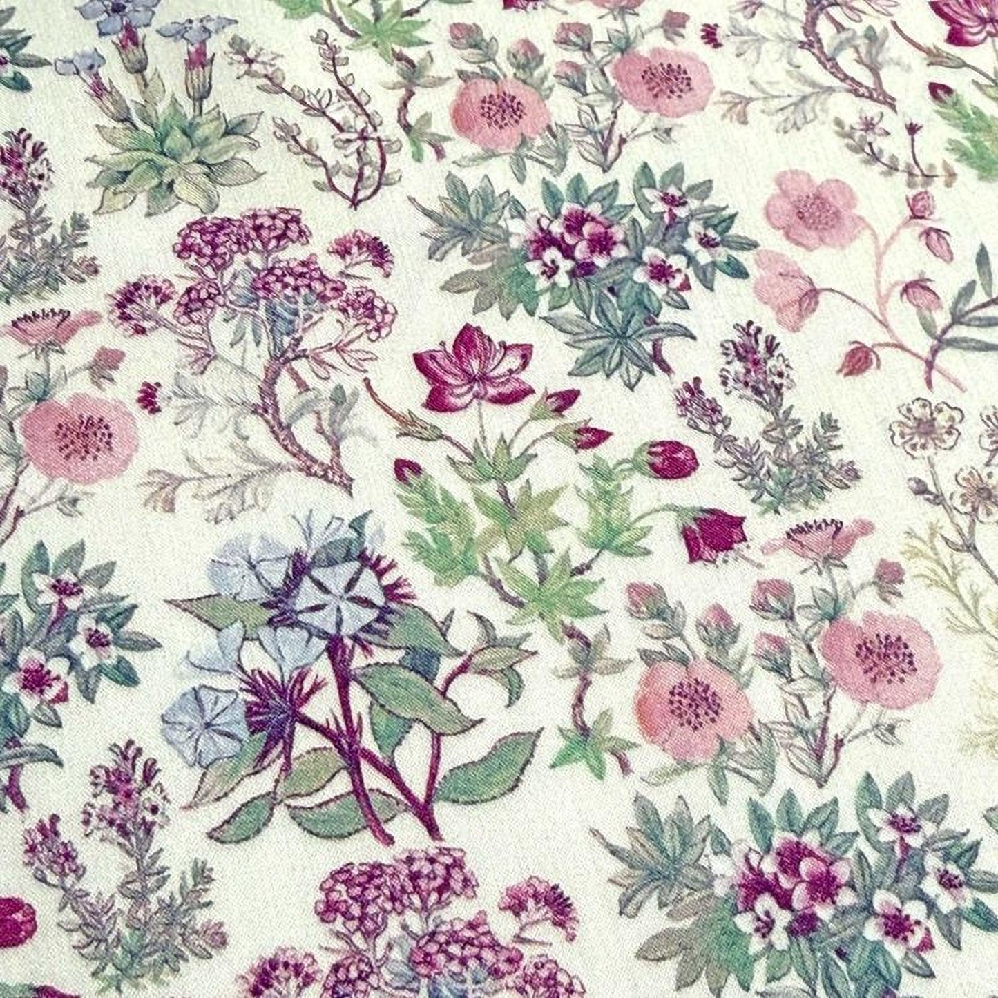 The image is a close-up of a fabric with a floral pattern, featuring various types of flowers and plants in shades of pink, purple, and green.