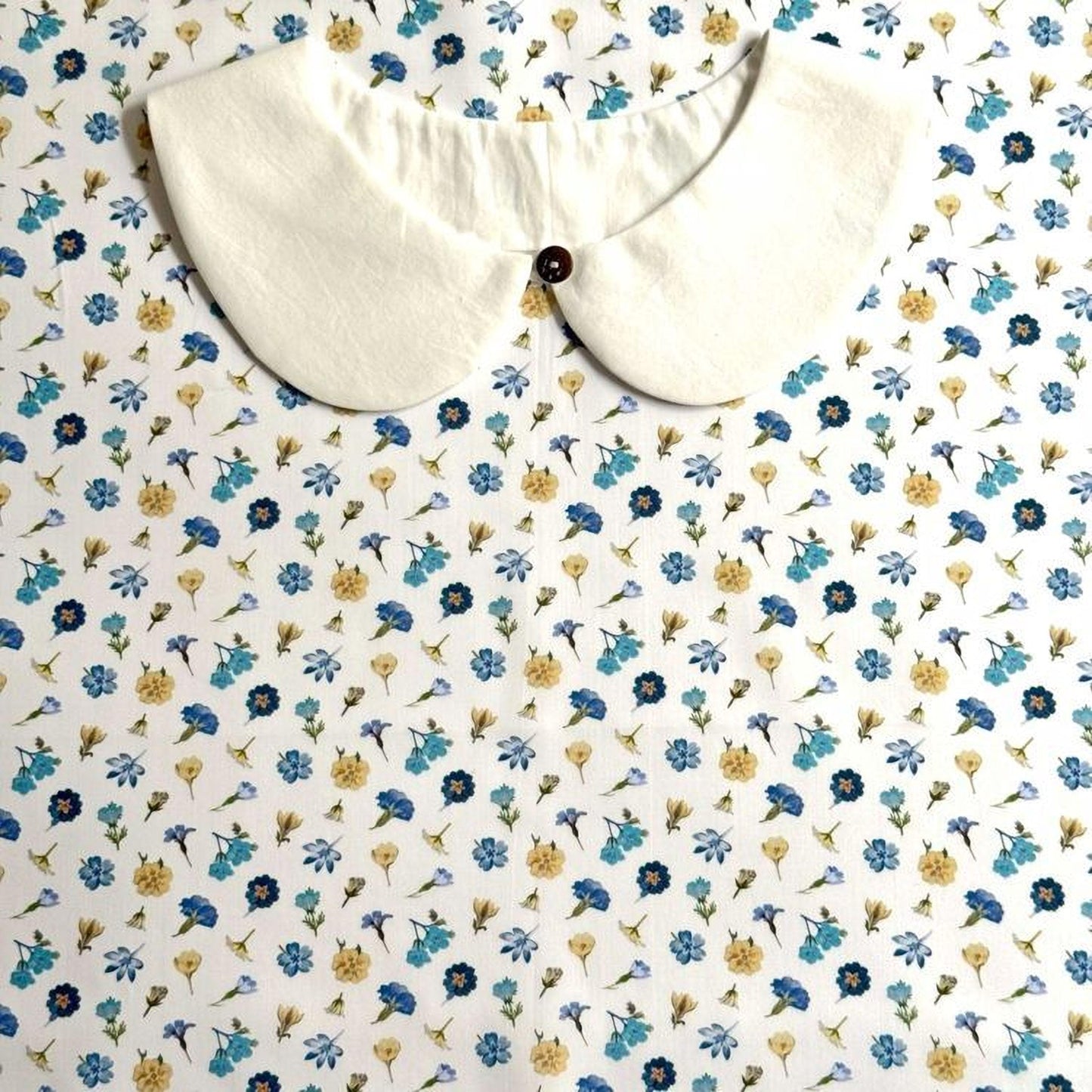 a white collar with a button, set against a background with a floral pattern in shades of blue and yellow.