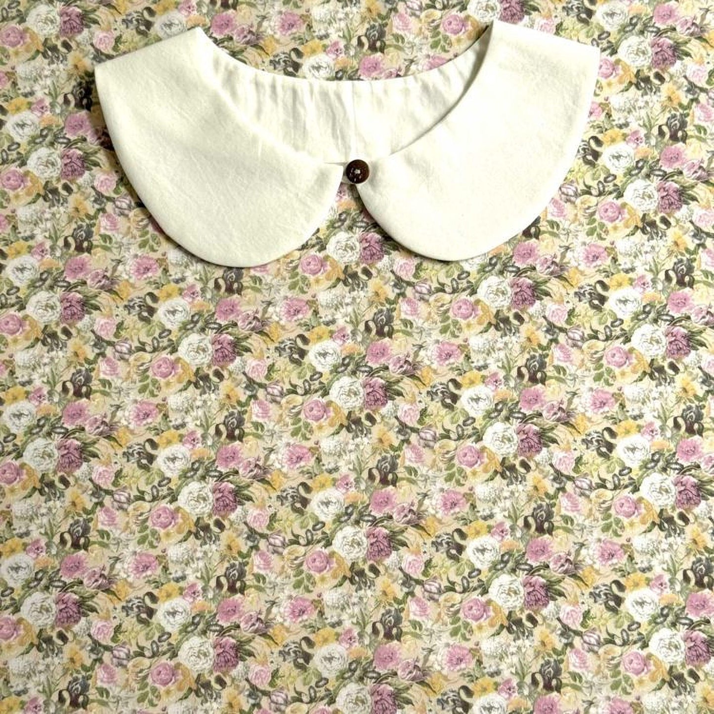 a white collar with a button, set against a background of a floral print fabric.