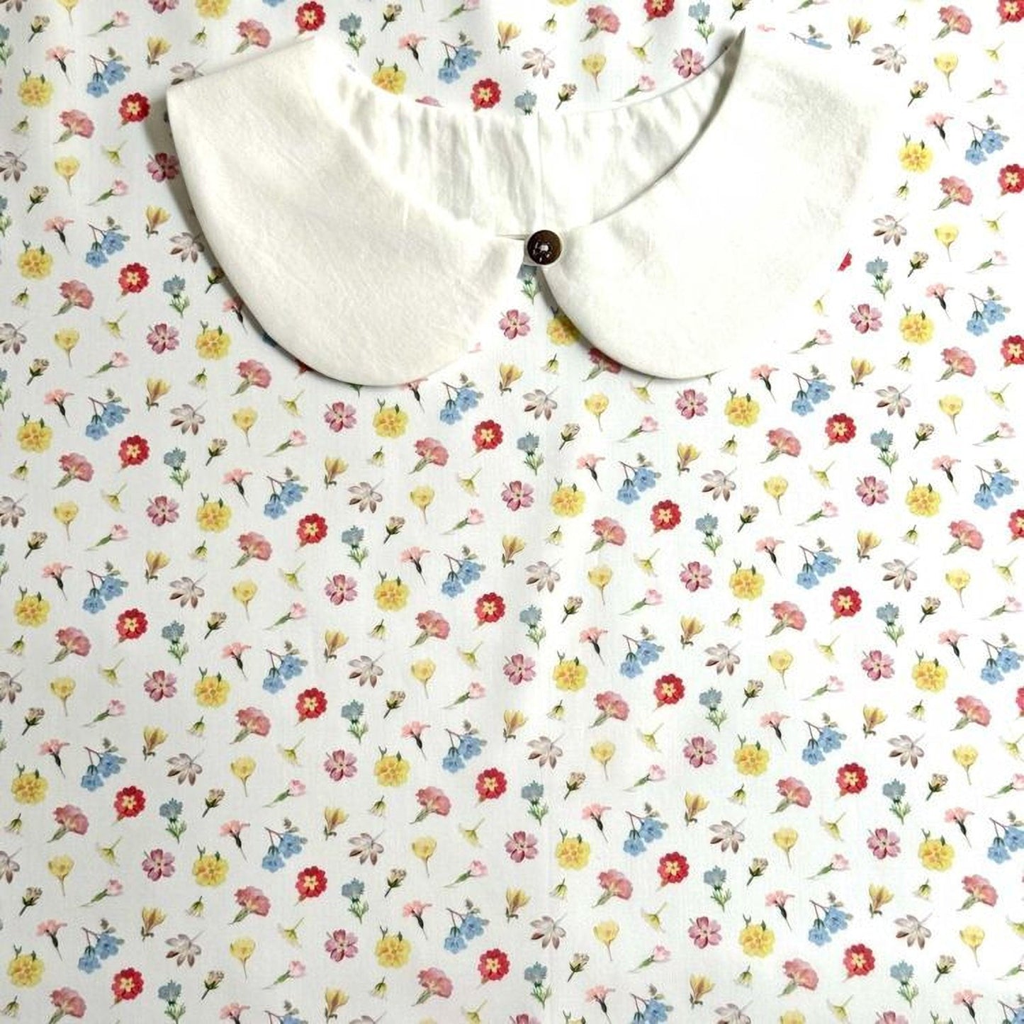 a white collar with a button, set against a background with a floral print.