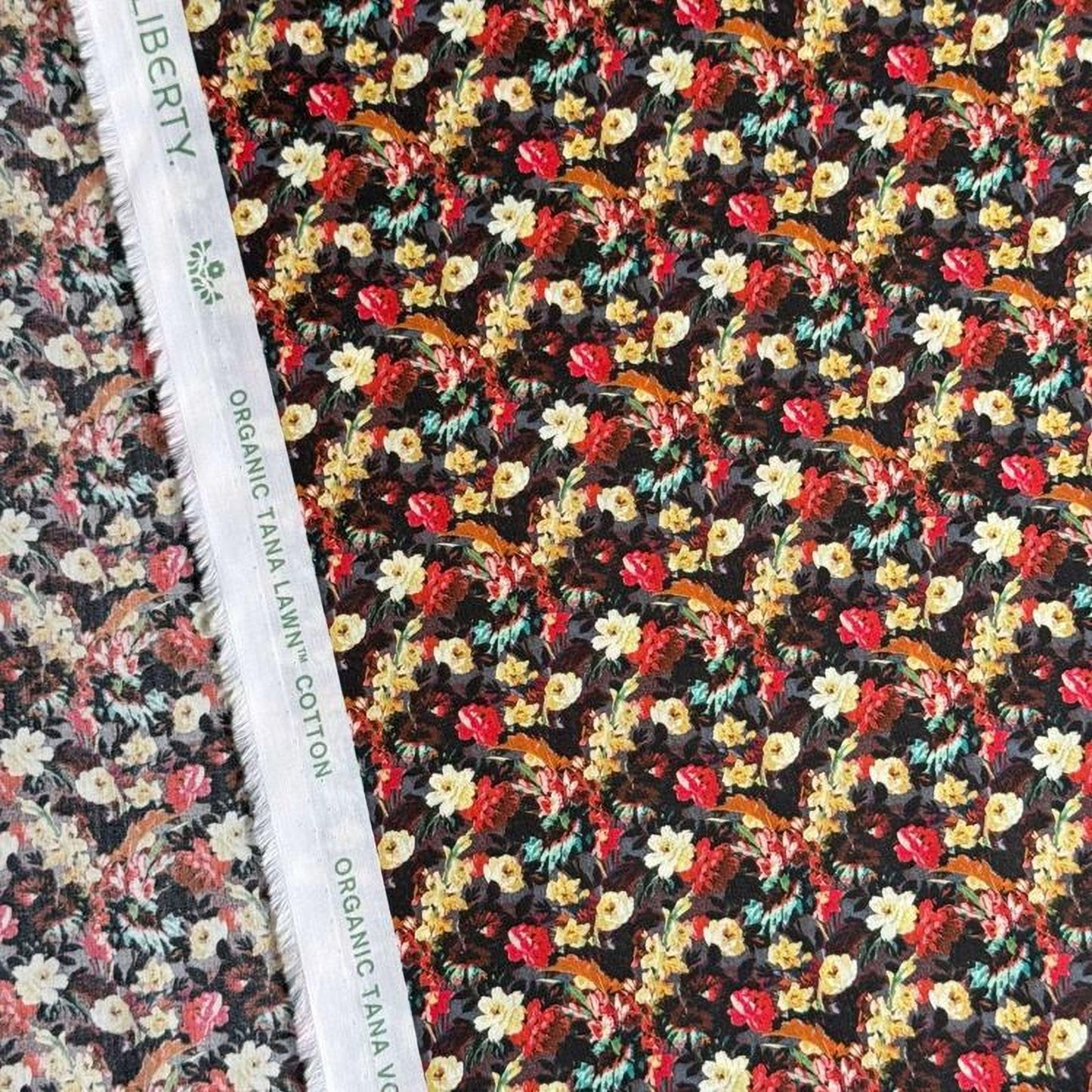 a close-up view of a fabric with a floral pattern, featuring a variety of colorful flowers and leaves. The fabric appears to be made of cotton and is displayed on a white fabric ruler.