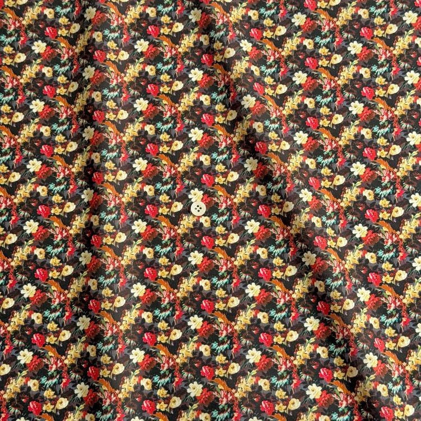 a close-up view of a fabric with a floral pattern. The fabric appears to be dark in color, with a repeating pattern of flowers in various colors, including red, yellow, and green. The pattern is intricate and detailed, creating a visually appealing design.