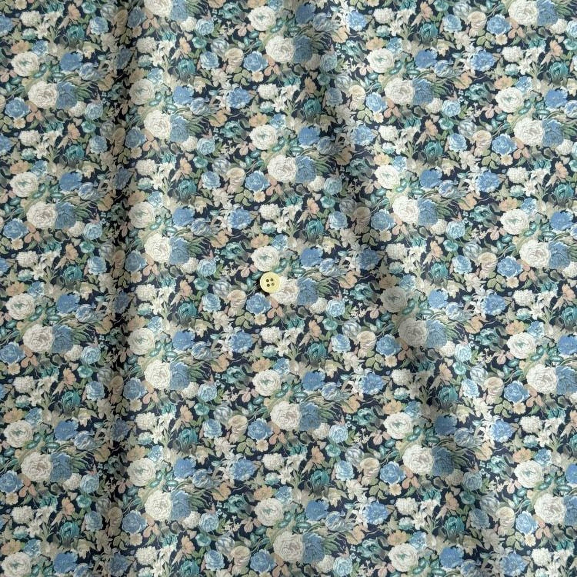 a close-up view of a fabric with a floral pattern, featuring a variety of colors including blue, green, and white. The fabric appears to be made of a soft, textured material, and there is a small yellow button visible in the center of the pattern.