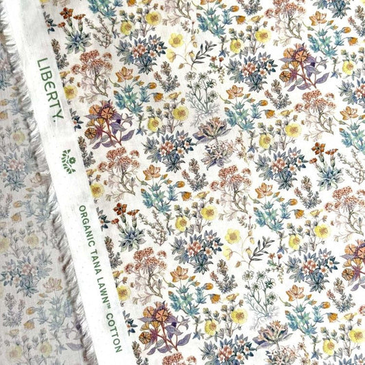 a close-up view of a fabric with a floral pattern. The fabric appears to be a white material with a variety of colorful flowers and leaves printed on it. The text "LIBERTY" and "ORGANIC TAN A LEW'N COTON" can be seen, indicating the type of fabric and its origin.