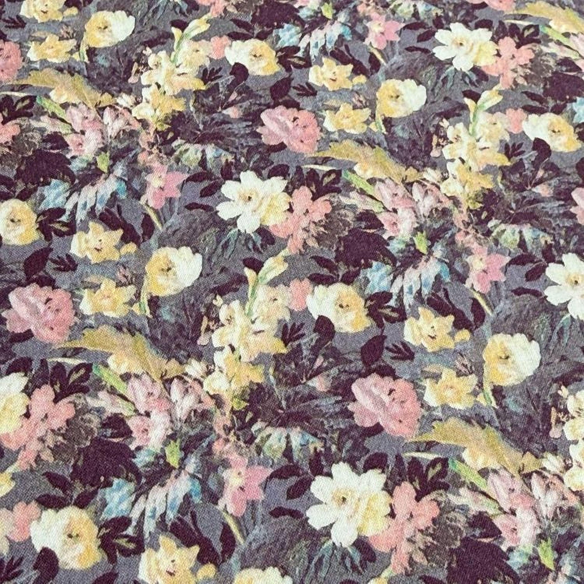 a close-up view of a fabric with a floral pattern. The fabric appears to be a dark-colored material with a variety of colorful flowers and leaves, including white, yellow, and pink flowers. The pattern is intricate and detailed, creating a visually appealing and textured appearance.