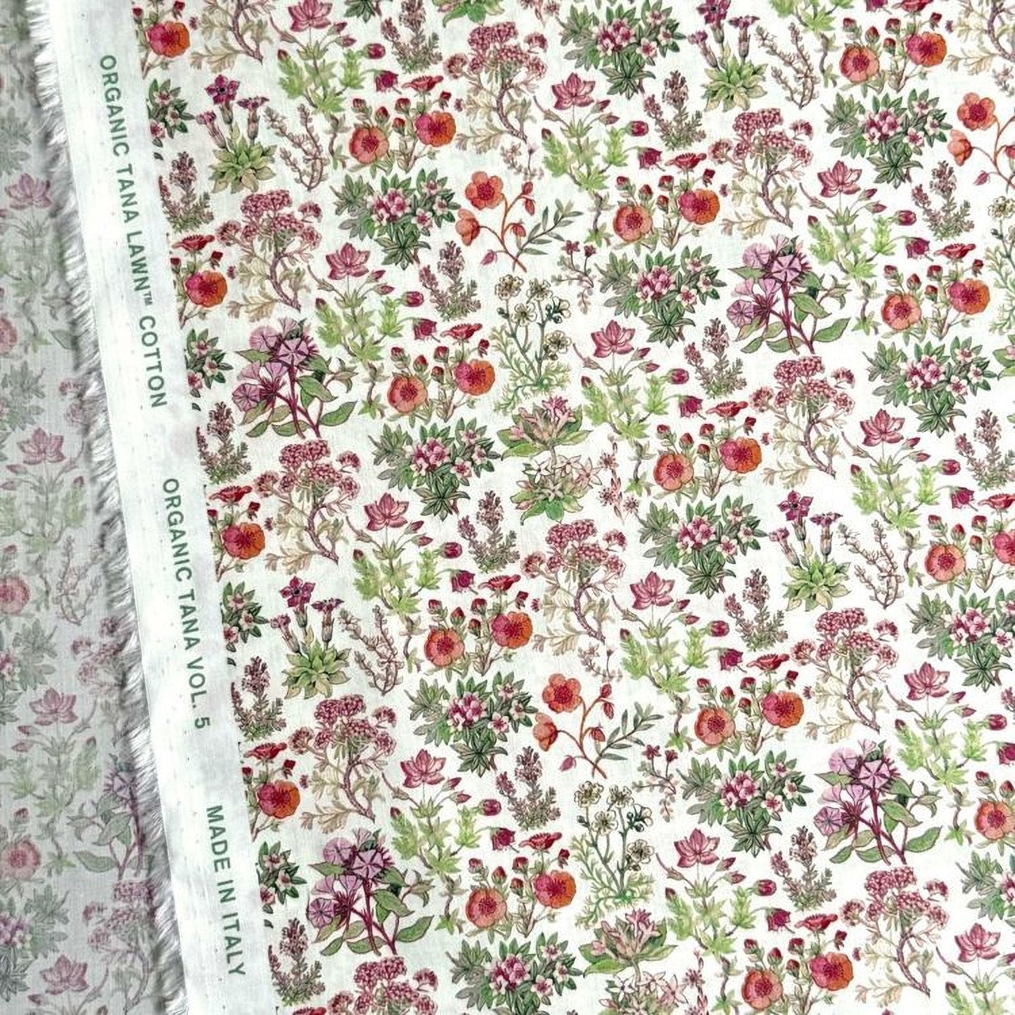 a close-up view of a fabric with a floral pattern. The fabric appears to be made of organic cotton and has a white background with a variety of colorful flowers and plants printed on it.