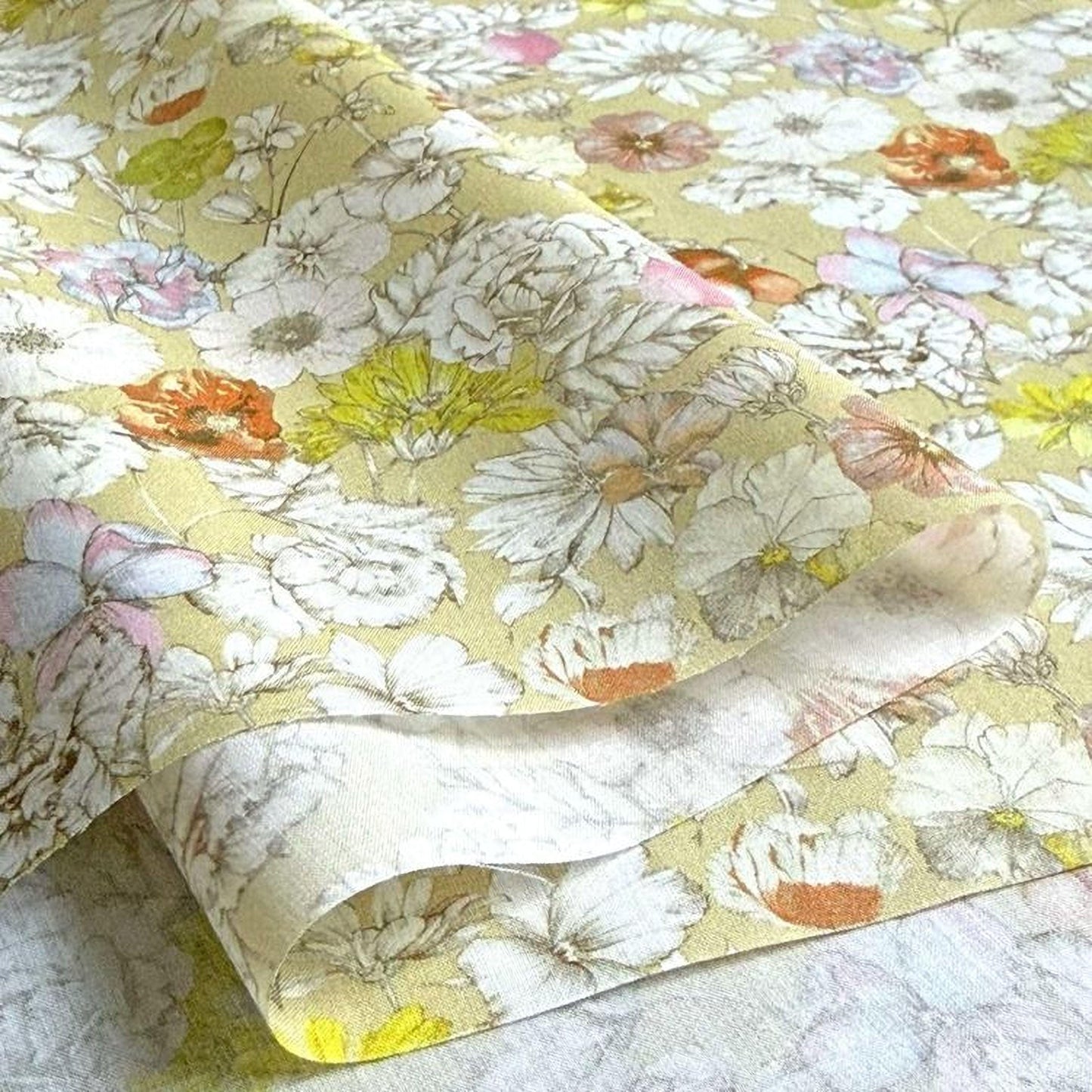 a close-up view of a fabric with a floral pattern, including various types of flowers in different colors such as white, yellow, orange, and pink. The fabric appears to be a piece of paper or a textile with a printed design.