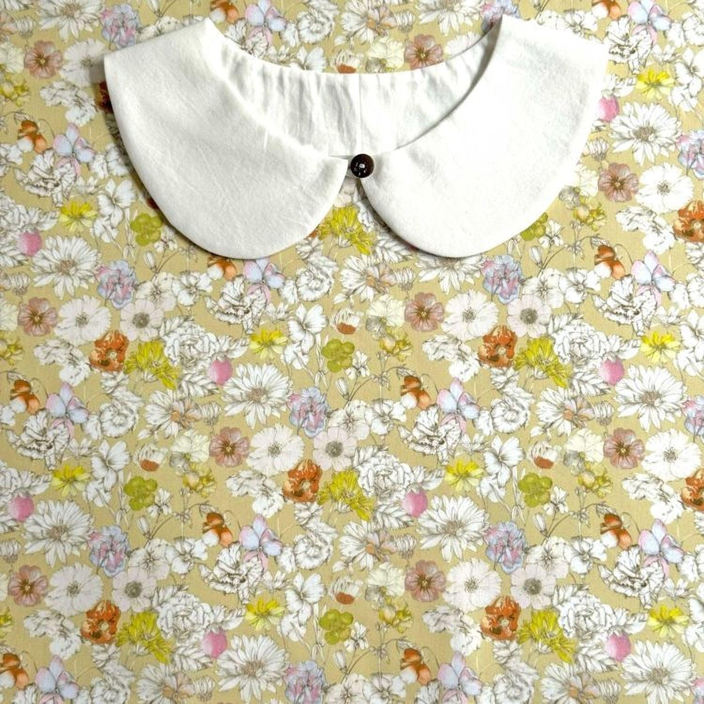 A white collar is placed on a floral print fabric.