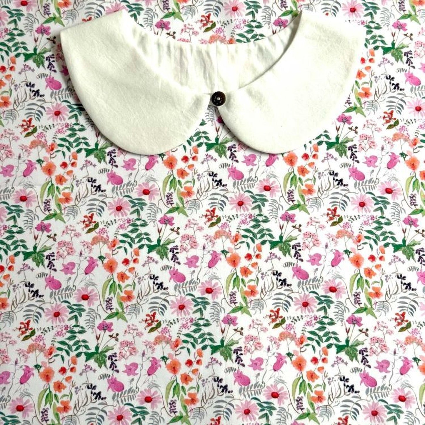 a white collar with a button, placed on a floral print fabric.