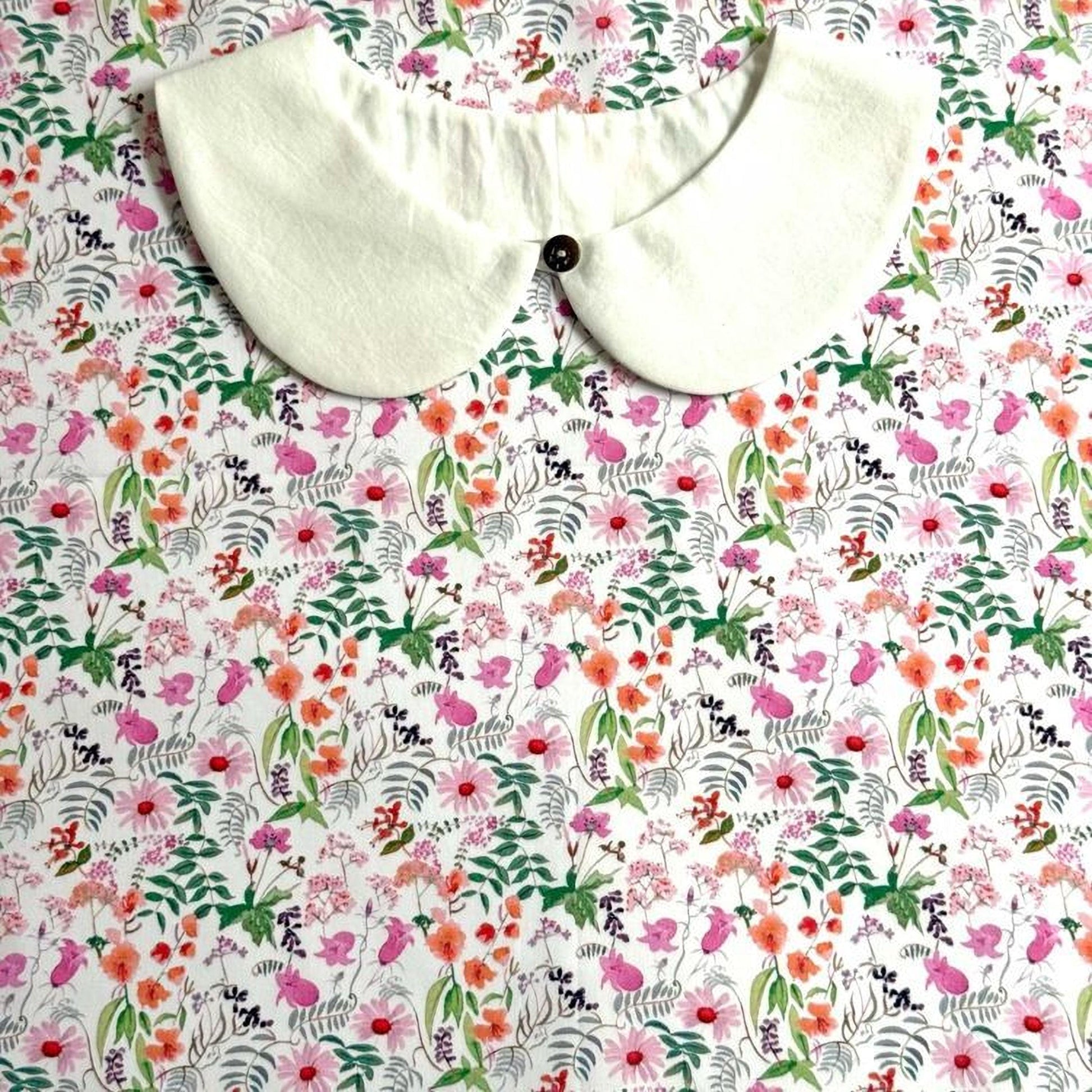 a white collar with a button, placed on a floral print fabric.